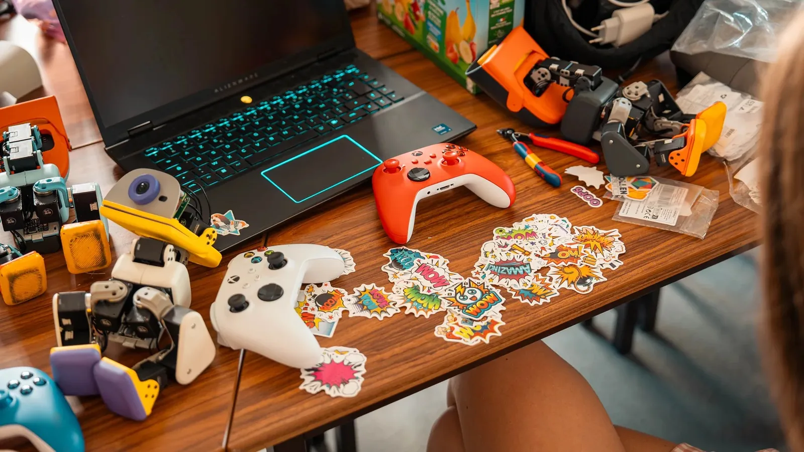 Microduck robots on a desk next to a laptop, game controllers and stickers