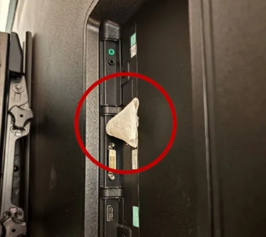 The back of a TV with a small tissue-wrapped device plugged in, circled in red